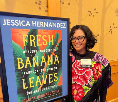 Dr. Hernandez wearing a floral huipil, standing next to a Fresh Banana Leaves book poster. 